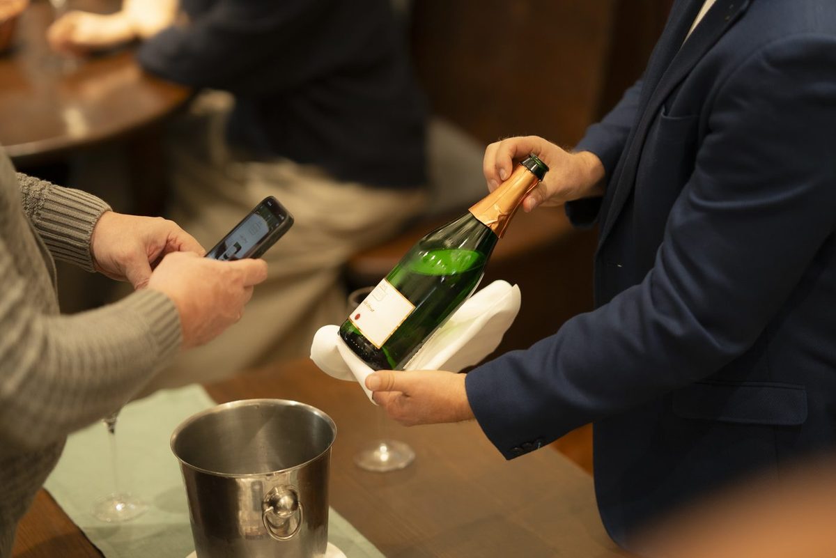 Eine Flasche Sekt wird am Tisch geöffnet, daneben der Kühler