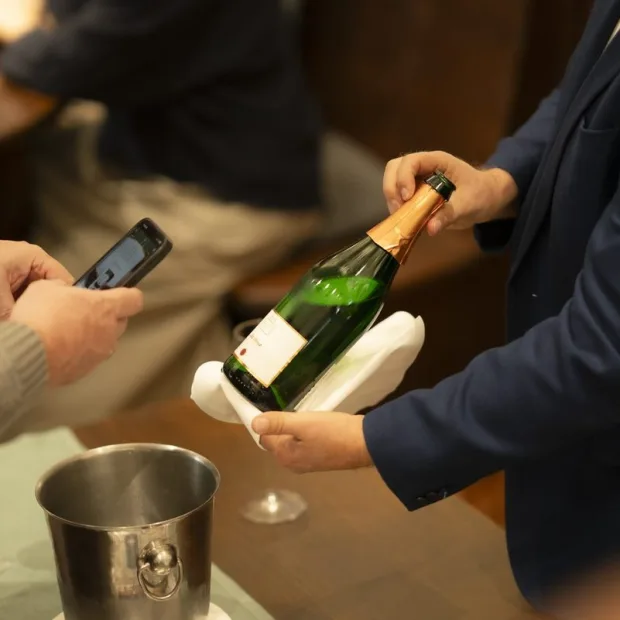 A bottle of sparkling wine being opened at the table, the cooler beside it