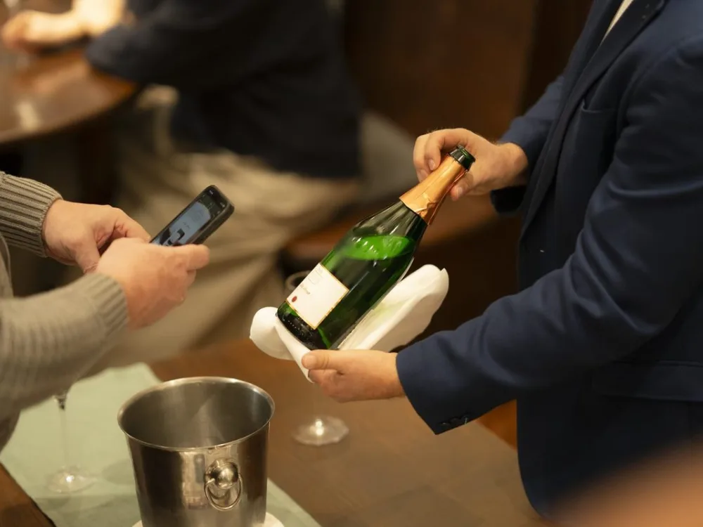 Eine Flasche Sekt wird am Tisch geöffnet, daneben der Kühler